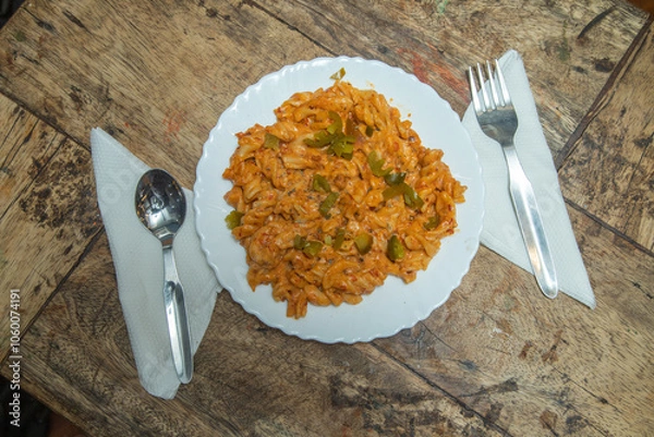 Fototapeta Spicy pasta with capsicum and place a spoon and fork, pasta placed in a wooden dining table, Italian spicy foods in India