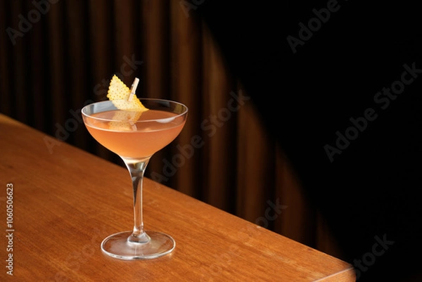 Fototapeta Bronx cocktail glass with orange peel slice on a wooden bar counter, background with copy space
