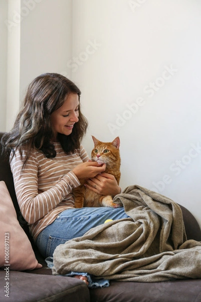 Obraz Brunette young woman playing with her rescue red cat at home. Copy space background.