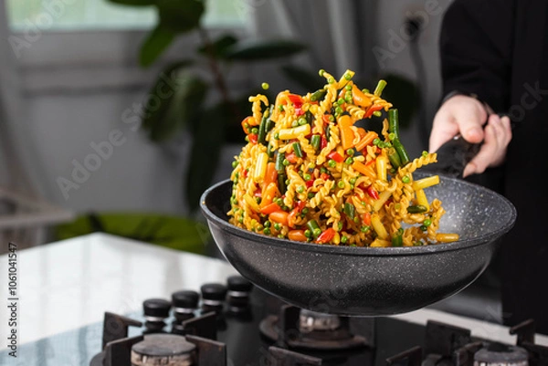 Obraz Close up of Chef cook hands cooking and toss roasted pasta, onion, pepper, carrot, vegetables, mushrooms, green peas, beans, garlic in frying wok pan on gas stove. Flying food levitation.