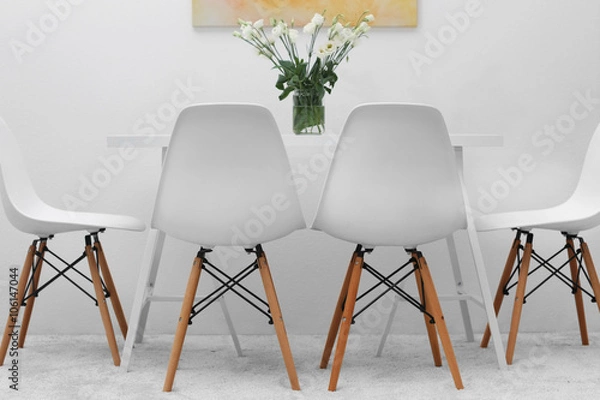 Fototapeta Modern dining room. White chairs and table with bouquet of flowers, abstract bright picture on the wall