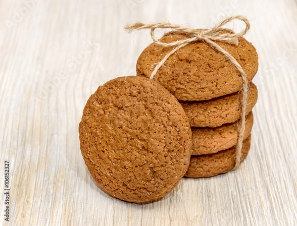Fototapeta Stack oatmeal cookies tied with thread on a wooden background