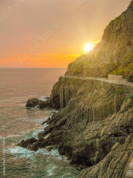 Fototapeta sunset on the rocky cliffs of the Italian riviera coastline as the sun sets over the ligurian sea. Tourists enjoy view walking along the famous path of love at sunset in Cinque Terre National park
