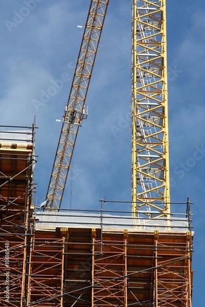Fototapeta Détail de deux grues sur un chantier de construction avec vue sur le bâtiment en cours de construction et les échafaudages