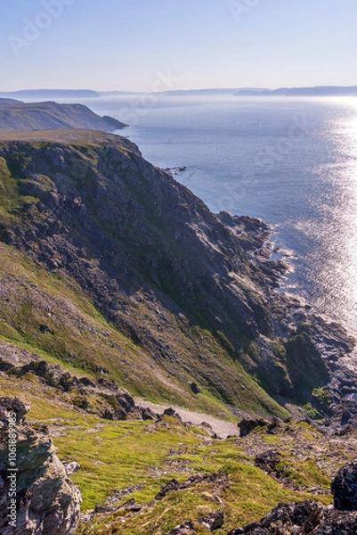 Fototapeta A dramatic view from the edge of a cliff, looking out over the vast, blue ocean shrouded in mist. The view of the Barents Sea opens from the Tanahorn cliff in Norway