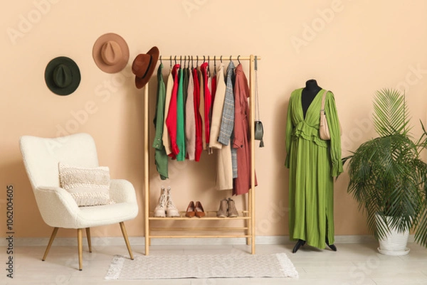 Fototapeta Rack with clothes, armchair and mannequin near beige wall in dressing room
