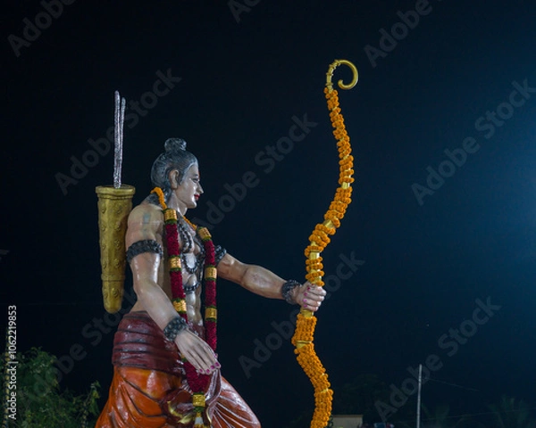 Fototapeta A statue of Lord Rama holding a decorated bow and arrow, adorned with garlands, symbolizing the victory of good over evil in Dussehra celebrations, associated with Ravana Vadh.