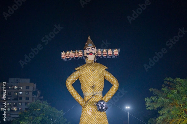 Fototapeta A tall, illuminated effigy of Ravana with multiple heads, symbolizing the Hindu festival of Dussehra, stands against a dark night sky, ready for celebration and burning. Ravan Dahan.