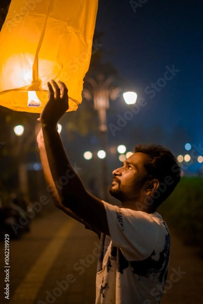 Fototapeta man releasing a glowing sky lantern at night, capturing the festive spirit of Diwali, symbolizing hope, light, and the triumph of good over evil. Ideal for themes of Diwali, celebration, and cultural 