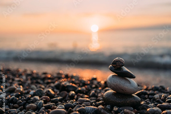 Fototapeta A pyramid of pebbles on the background of the sea and sunset. Sea pebbles on the background of waves. Beautiful sea coast. A pebble beach. Summer sunset at sea