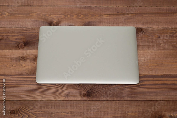 Obraz Closed silver laptop on brown wooden table