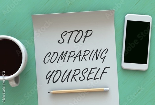 Fototapeta STOP COMPARING YOURSELF, message on paper, smart phone and coffee on table