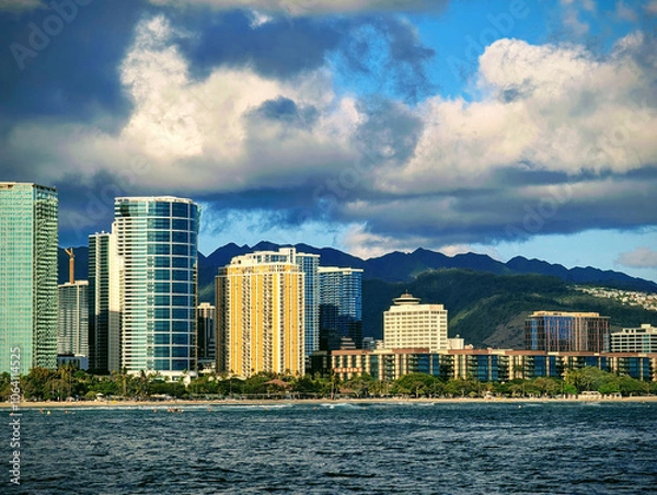 Fototapeta Vibrant skyline of Honolulu with modern skyscrapers and lush mountains under a dramatic sky during the late afternoon