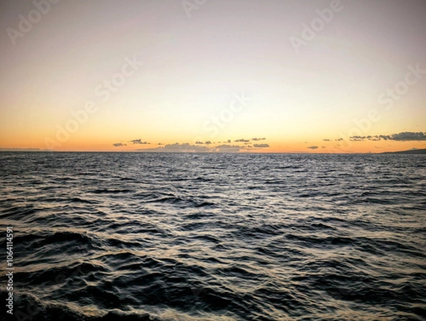 Fototapeta A tranquil sunset over the calm ocean, with gentle waves reflecting warm colors on the water in a serene evening atmosphere