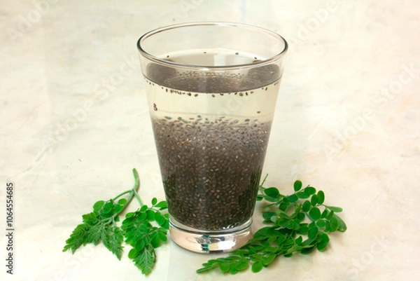 Fototapeta A glass of chia seeds soaked overnight in water, with fresh moringa leaves beside it for a natural, vibrant touch. This nutrient-rich, hydrating superfood drink is perfect for wellness and health-focu