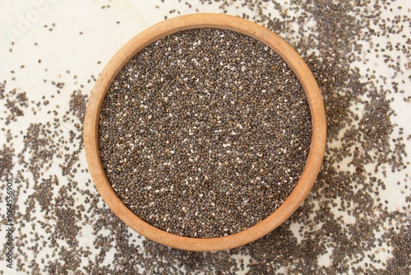 Fototapeta Chia seeds in a bowl with some scattered on the ground, showcasing their raw, natural texture. Ideal for health, nutrition, and superfood content.