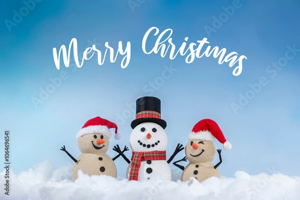 Obraz A joyful snowman and two sandy snowmen pose together for a Christmas and New Year celebration! With a snowy backdrop and blue sky, this mix of winter and beach vibes brings a fresh holiday twist.