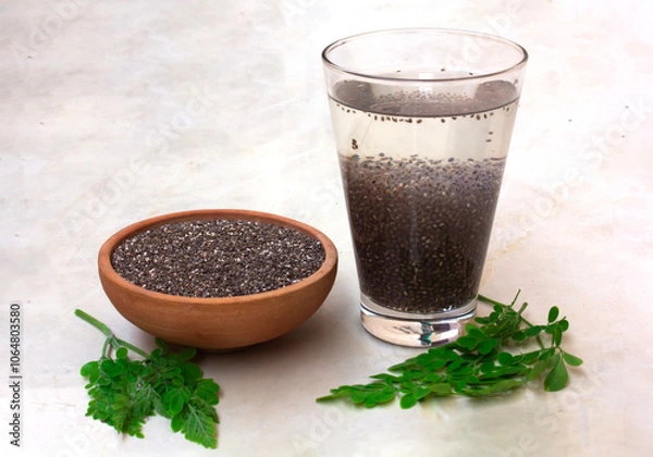 Fototapeta A glass filled with soaked chia seeds alongside a bowl of dry chia seeds, with moringa leaves scattered on the ground, highlighting the nutritious qualities of these superfoods.