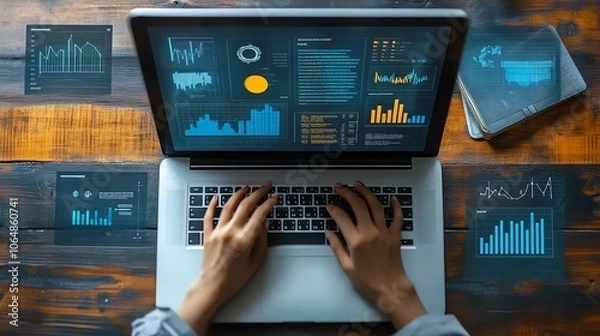 Fototapeta Hands typing on laptop with data analytics and financial graphs on screen and desk.