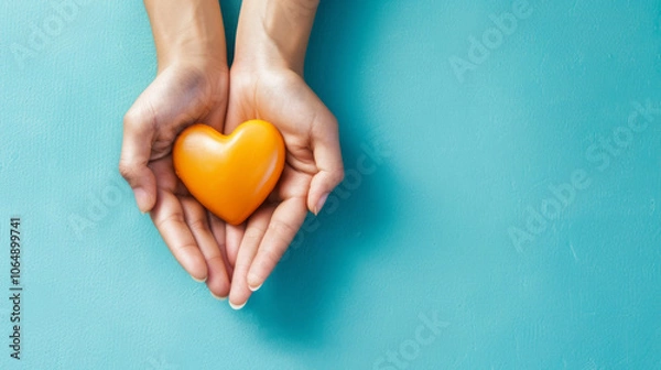 Fototapeta Hands holding an orange heart on a blue background as a symbol of volunteer appreciation and community support