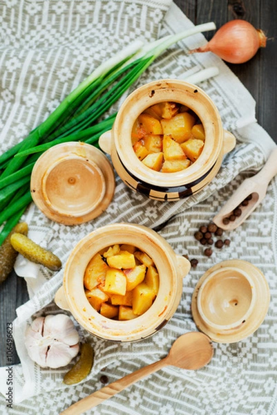 Fototapeta 
National Russian , Ukrainian and Belarusian cuisine , baked potatoes with meat in the pot , onion , pepper, garlic , pickled cucumber and spices on a wooden background