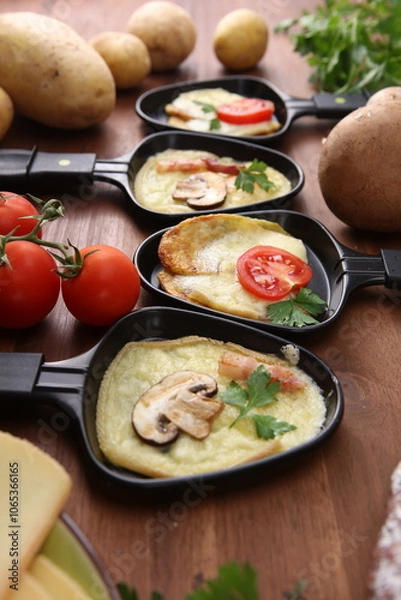 Fototapeta Delicious traditional Swiss melted raclette cheese served in individual skillets with salami and bacon