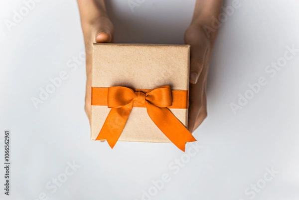 Obraz Cartboard gift box with orange ribbon and bow in hands on white background isolated