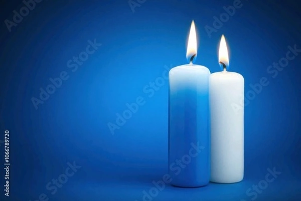 Fototapeta Two candles, one blue and one white, glow softly against a blue backdrop, creating a tranquil ambiance perfect for relaxation