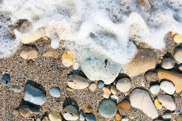 Fototapeta sassi vari colori sulla sabbia in riva al mare levigati bagnati dalle onde