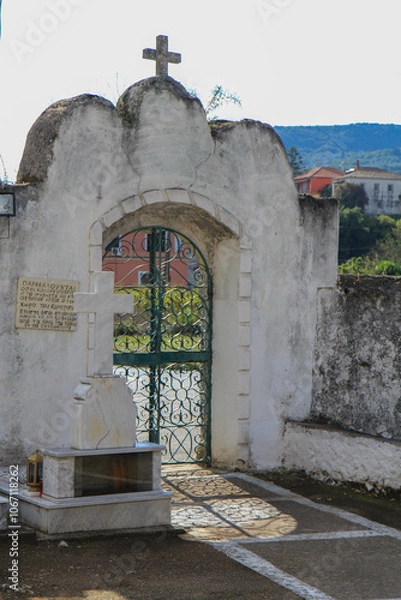 Fototapeta Ornate Stone Gate Structure with a Cross on Top: Concrete and Metal Gate with Intricate Ornaments on a Greek Island