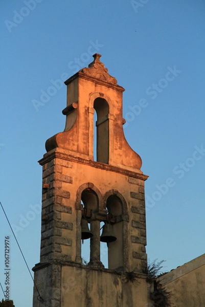 Fototapeta Concrete Bell Tower with Copper Green Bells: Street-Level View of a Sunlit Structure on a Greek Island