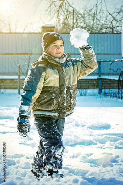 Fototapeta Baby boy walking at snowfall. Child in winter clothes playing with snow. boy making snowball outdoor. Boy playing snowballs in winter park. Christmas winter fun. toned