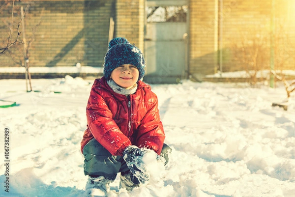 Fototapeta Excited Child playing with snow on white snow background. smiling boy catching snowflakes. Funny little boy in blue winter clothes walks during a snowfall. Outdoors winter activities for kids. toned