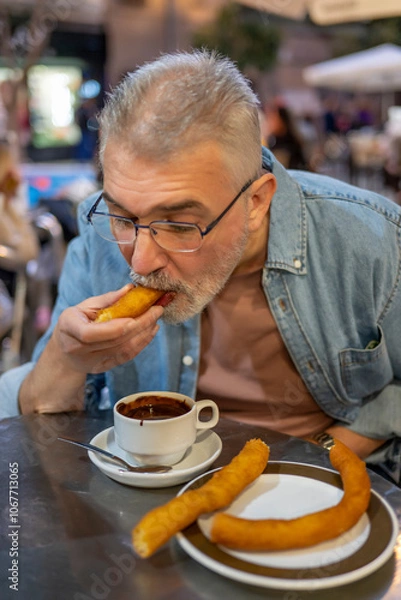 Fototapeta Senior man enjoying churros dipped in chocolate, savoring a quiet moment in a café