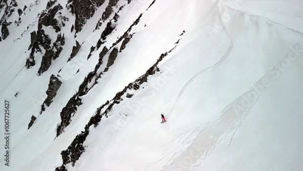 Obraz single snowboarder glides across a steep, open face of pure snow, framed by dark rocky outcrops.
