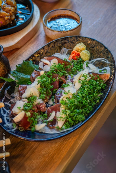 Fototapeta Grilled straw bonito, a signature dish from Kochi Prefecture, served sliced ​​with green onions, ginger, garlic and a special Ainanjo sauce.