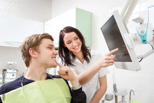 Fototapeta Young man on a review of a dentist, sitting in a chair. Dentist Explaining X-Ray on computer for patient in a dental clinic