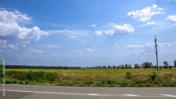Fototapeta Expansive rural landscape with a clear sky and distant trees along a quiet road on a sunny day