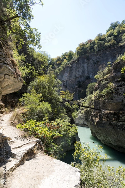 Fototapeta Osumi, Albania - August 15 2024: Small bridge (Ura e Vjeter e Zaberzanit) crossing the Osumi River Canyon. Beautiful views on famous gorge and river.