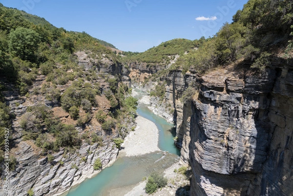 Fototapeta Osumi Gorge, Albania - August 15 2024: Stunning view of Osumi Canyon (Albanian: Kanioni i Osumit), showcasing the breathtaking cliffs, vibrant greenery, and winding river through dramatic landscape.