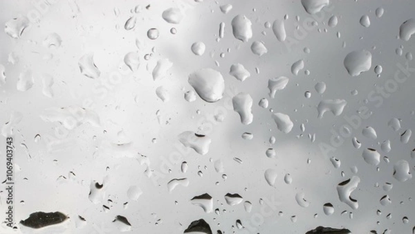 Fototapeta Raindrops cascading on a window, creating a blurred view of the outdoors during a cloudy day in a tranquil setting