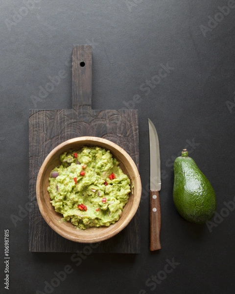 Fototapeta wooden bowl of guacamole and its ingredients on black background from above 