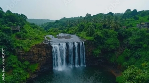 Fototapeta A serene waterfall cascading into a lush green landscape, surrounded by hills and trees.