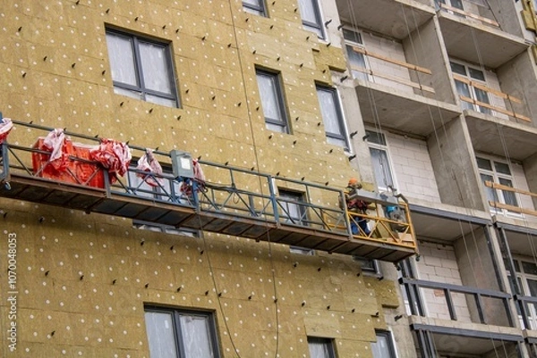 Fototapeta A man works on scaffolding located on the side of a building
