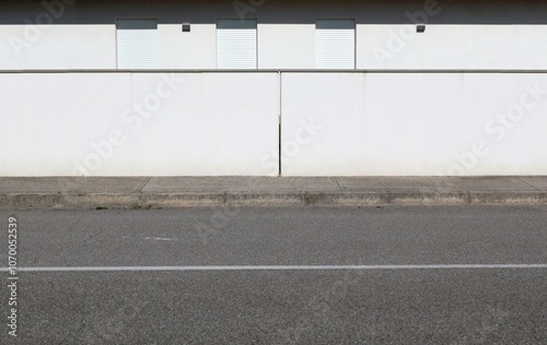 Fototapeta White plaster fence of modern house with closed shutters  behind. Cement sidewalk and asphat road in front. Background for copy space
