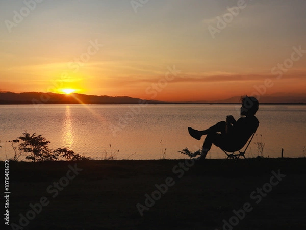 Fototapeta Silhouette of a man sitting on a chair at sunset.
