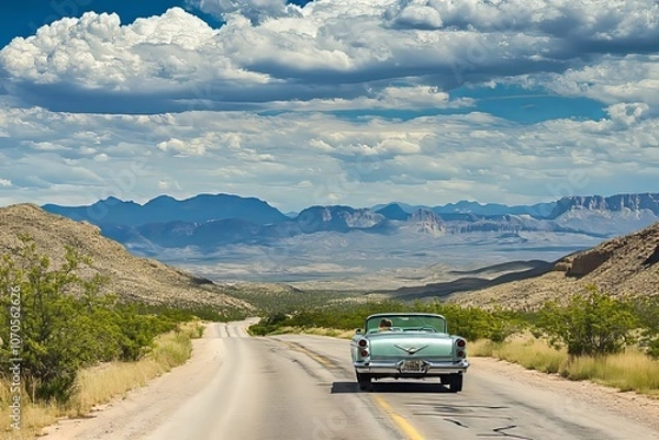 Fototapeta Classic car cruising down a scenic highway in the mountains on a sunny day under a blue, cloud-filled sky. Generative AI