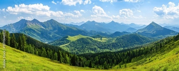 Fototapeta A panoramic view of lush green hills and mountains under a bright blue sky with fluffy clouds, showcasing stunning natural beauty.