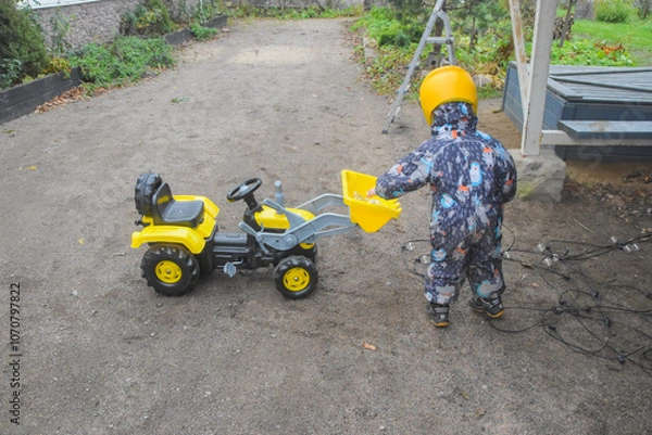 Fototapeta a child boy on a wheeled bulldozer tractor electrical work bulbs and light, photo without filters