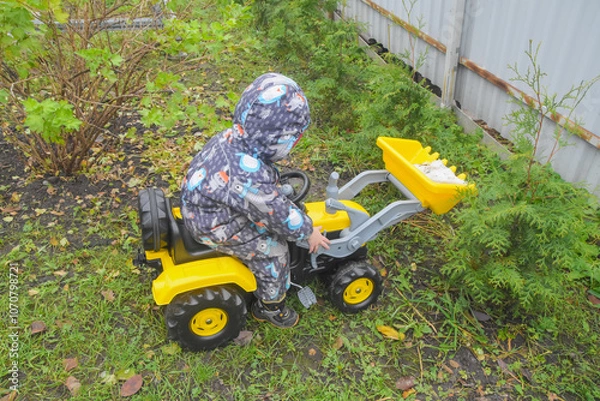 Fototapeta a child boy on a wheeled bulldozer tractor removes snow with a snow plow, photo without filters